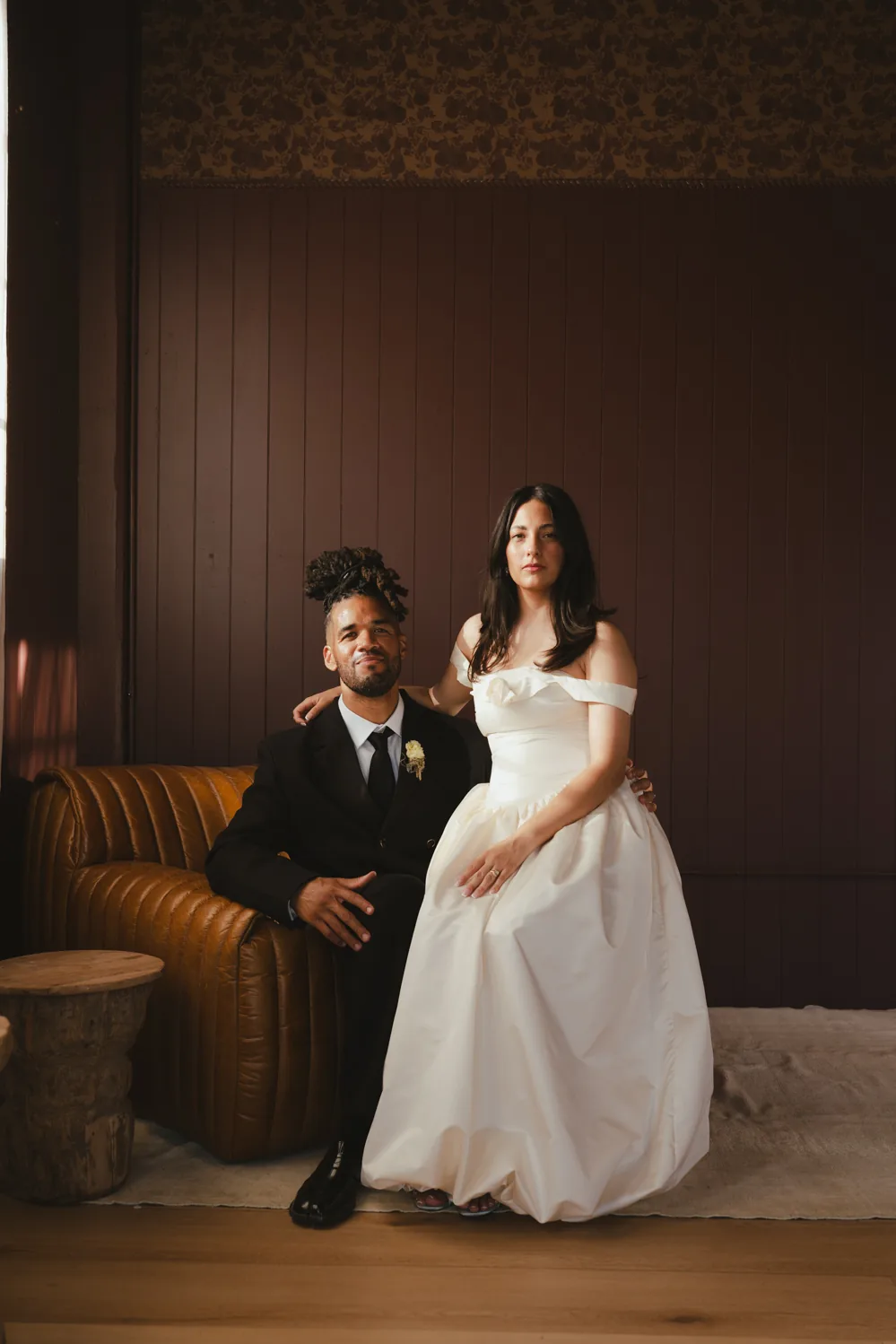 Couple in wedding attire seated together in a softly lit room